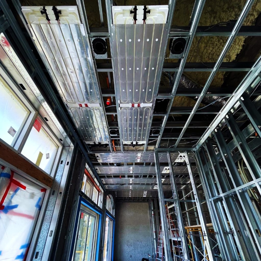 Radiant ceiling panels installed in between metal furring channels. Ray Magic® NK radiant ceiling panels provide hydronic heating and cooling.